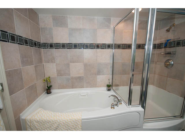Furnished bathroom with white tub, glass shower, and beige tile walls. - 2706 -198 Aquarius Mews, Vancouver Downtown