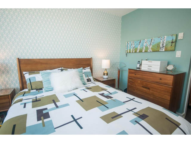 Bright bedroom with geometric patterned bedding and teal walls, featuring a wooden headboard and nightstand.