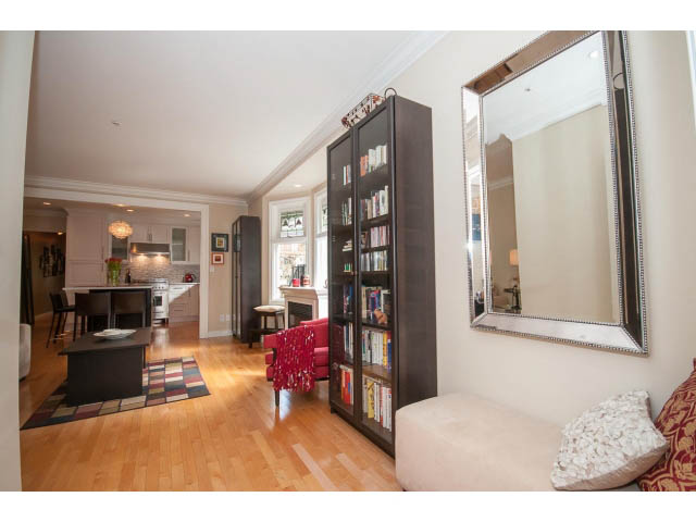 Furnished living room with hardwood floors, large mirror, and bookshelf. - 3 - 2535 West 6th Ave, Vancouver West Side