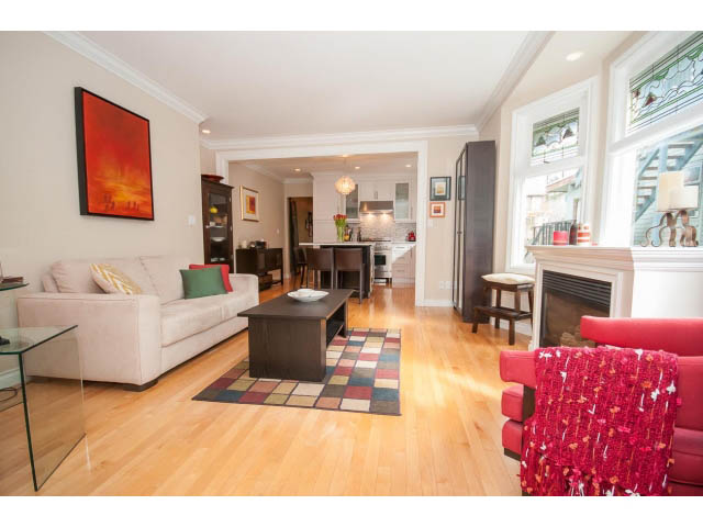 Bright living room with hardwood floors and a red accent wall, leading to a kitchen with stainless steel appliances and a...
