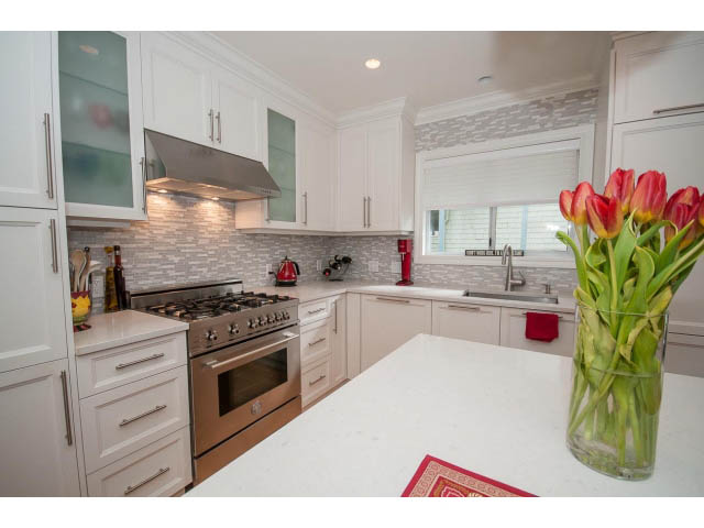 Bright kitchen with white cabinetry, granite countertops, and a red tulip vase on the counter. - 3 - 2535 West 6th Ave, Vancouver West Side