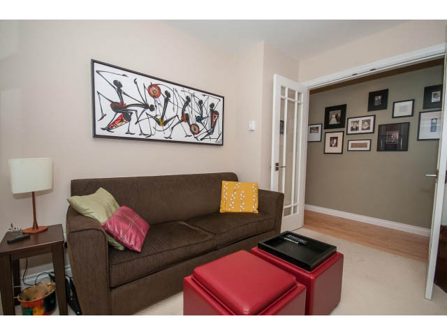 Furnished living room with a bold abstract painting, red ottoman, and brown couch. - 3 - 2535 West 6th Ave, Vancouver West Side