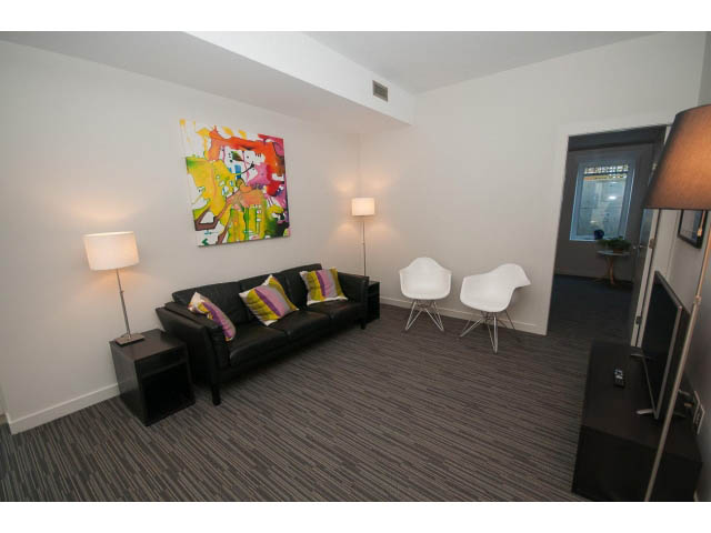 Furnished living room with modern furniture, abstract art, and a glass door leading to another room. - Suite - 1252 Duncan St, West Vancouver