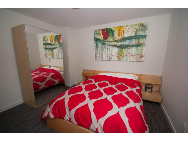 Bright bedroom with red patterned bedding and abstract art on the wall. - Suite - 1252 Duncan St, West Vancouver