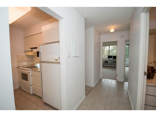 Bright kitchen with white cabinetry and tiled countertops, leading to a cozy living area. - 606 - 2020 Fullerton Ave, North Vancouver