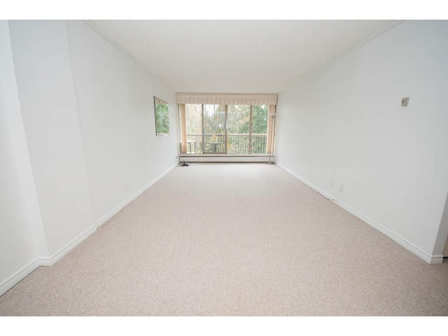 Bright living room with carpeted floors and a large window showing trees outside. - 606 - 2020 Fullerton Ave, North Vancouver