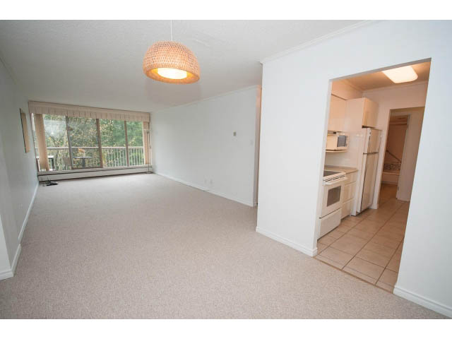 Bright living room with carpeted floors, large window, and wicker pendant light. - 606 - 2020 Fullerton Ave, North Vancouver