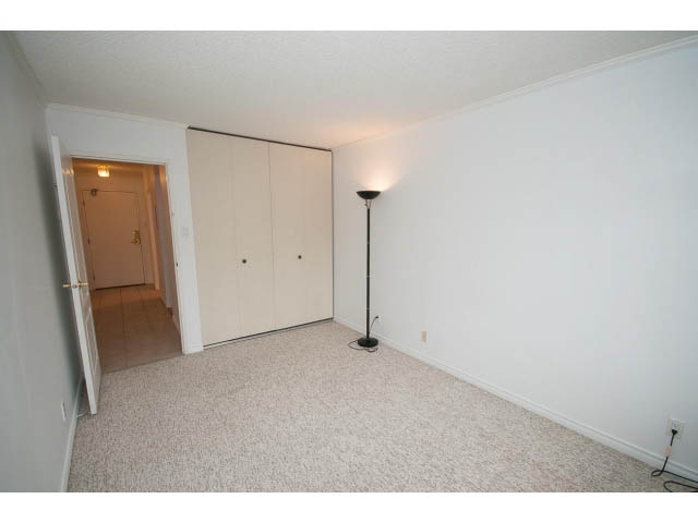 Bright living room with white walls and carpeted floor, featuring a lamp and closet. - 606 - 2020 Fullerton Ave, North Vancouver