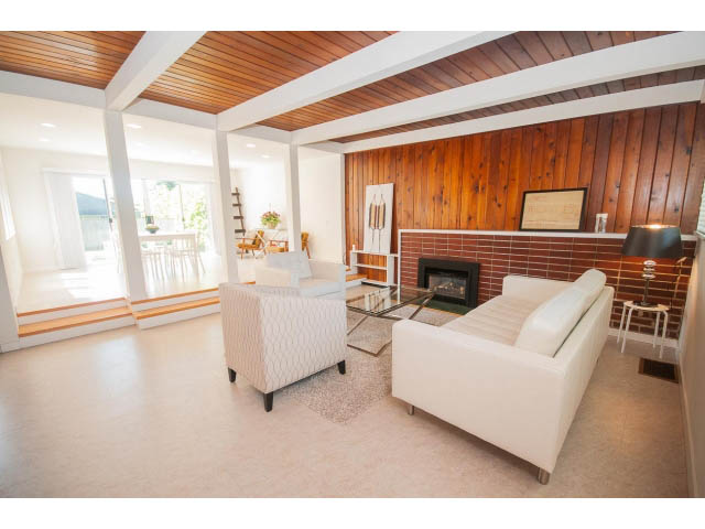 Bright living room with white leather furniture, wood-paneled walls, and a fireplace. - 753 East 15th St, North Vancouver