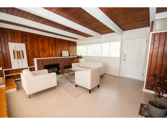 Spacious living room with white furniture, wooden beams, and a brick fireplace. - 753 East 15th St, North Vancouver