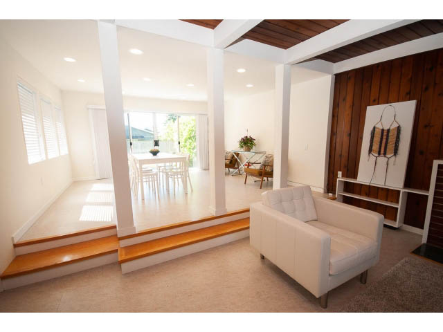 Bright living room with white furniture, wooden accents, and a view of the kitchen. - 753 East 15th St, North Vancouver