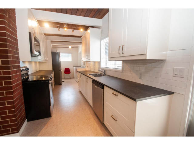 Bright kitchen with white cabinets, black countertops, and brick wall accent. - 753 East 15th St, North Vancouver