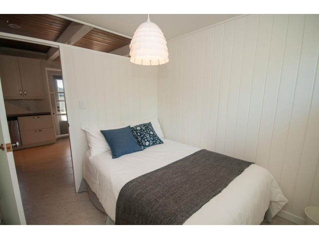 Furnished bedroom with white panel walls, wooden ceiling, and a modern pendant light. - 753 East 15th St, North Vancouver
