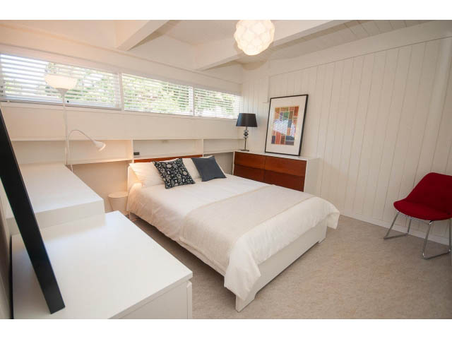 Bright bedroom with white walls, wooden accents, and a red chair. - 753 East 15th St, North Vancouver