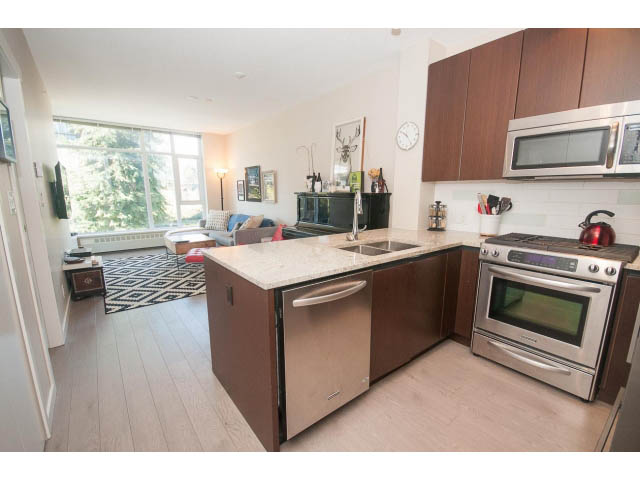 Bright kitchen with stainless steel appliances, hardwood floors, and a city view. - 203 - 135 West 2nd Street, North Vancouver