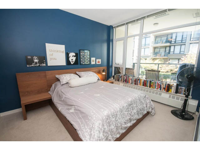 Bright bedroom with wooden bed, city view, and bookshelf. - 203 - 135 West 2nd Street, North Vancouver