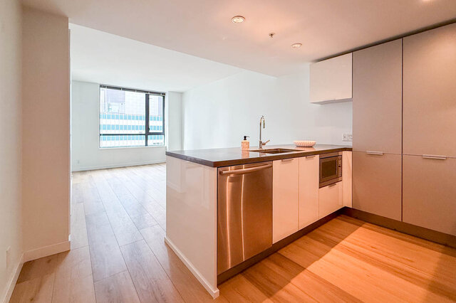 Modern kitchen with stainless steel island, dark countertops, and light hardwood floors. - 1904-788 Richards Street, Vancouver Downtown