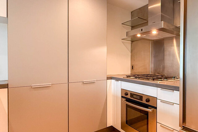 Modern kitchen with white flat-panel cabinets, stainless steel range hood, gas cooktop, and built-in oven.