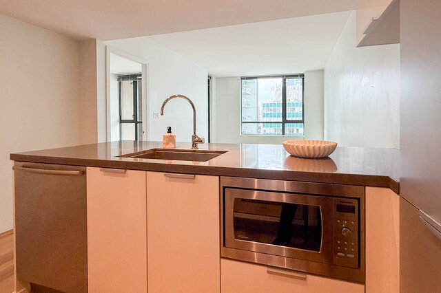 Modern kitchen island with dark stone countertops, light wood cabinetry, and a city view through the window.