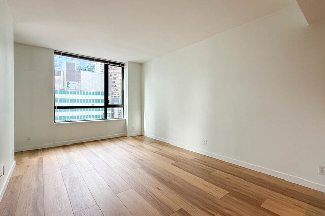 Bright empty living room with light hardwood floors and a window framing a downtown city view. - 1904-788 Richards Street, Vancouver Downtown