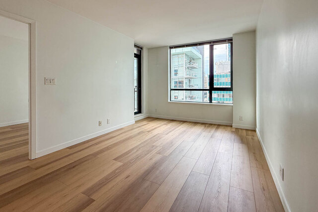 Empty living room with light hardwood floors and a large window framing a downtown city view. - 1904-788 Richards Street, Vancouver Downtown