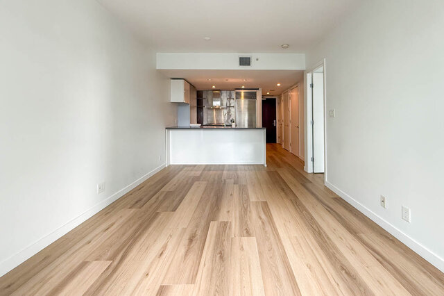 Bright living room with light hardwood floors and an open view to a white kitchen island. - 1904-788 Richards Street, Vancouver Downtown