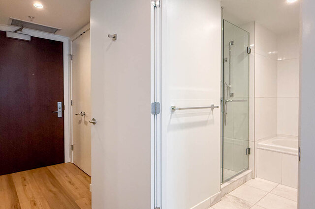 Bathroom with glass shower enclosure and white tile, adjacent to hardwood-floored entry. - 1904-788 Richards Street, Vancouver Downtown