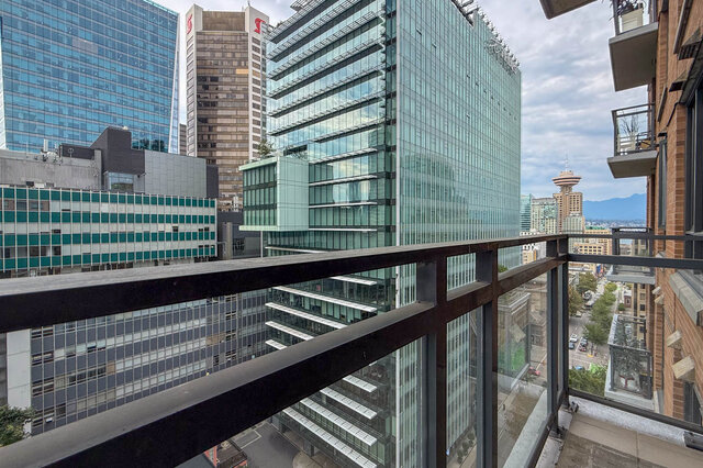 Balcony with dark metal railing overlooking a dense glass high-rise skyline and distant mountains. - 1904-788 Richards Street, Vancouver Downtown