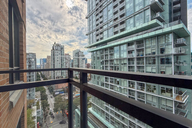 Balcony with black metal railing overlooking a dense downtown skyline of glass towers and a tree-lined street.