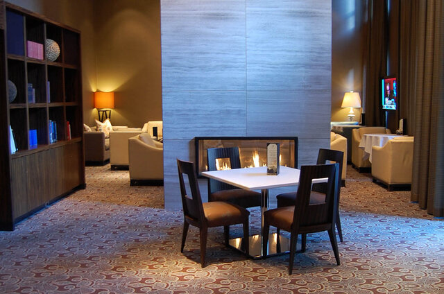 Furnished lounge with a white dining table, dark wood chairs, and a built-in fireplace against a light stone wall.