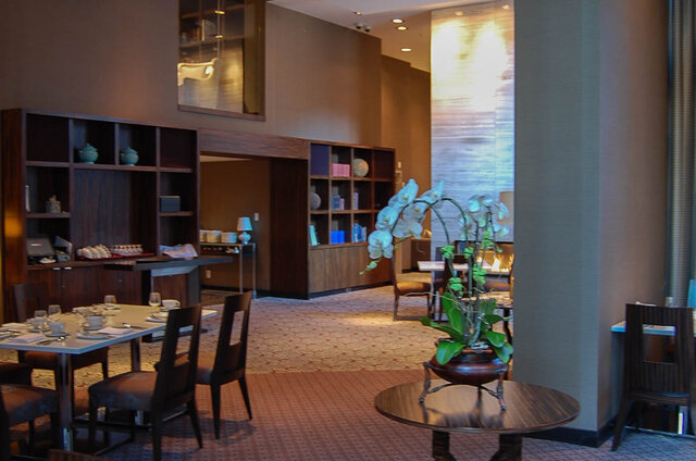 Furnished dining lounge with set table, dark wood built-in shelving, and a white orchid centerpiece on a round table.