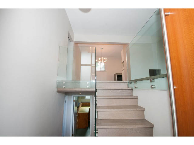 Modern staircase with glass railings and wooden steps leading to a bright upper level. - 3188 St. Andrews Ave, North Vancouver