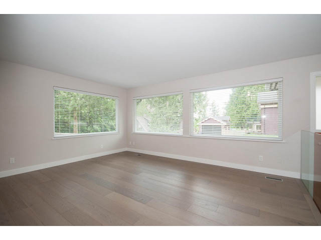 Bright living room with hardwood floors and large windows offering a view of greenery. - 3188 St. Andrews Ave, North Vancouver