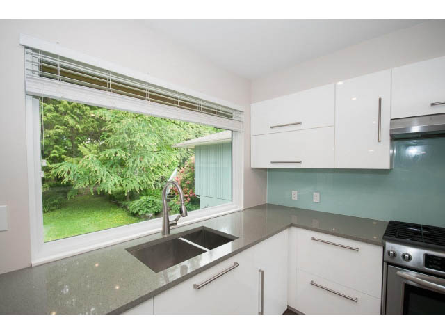 Bright kitchen with modern white cabinets, green backsplash, and large window overlooking greenery. - 3188 St. Andrews Ave, North Vancouver