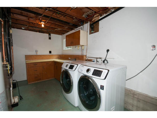 Laundry room with white washers and dryers, wooden cabinets, exposed ceiling beams. - 3188 St. Andrews Ave, North Vancouver