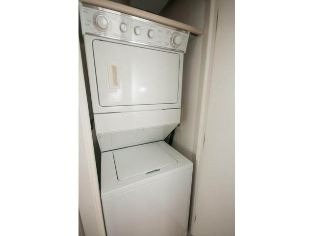 Bright laundry room with stacked washer and dryer, white cabinetry. - 701 - 151 West 2nd Street, North Vancouver
