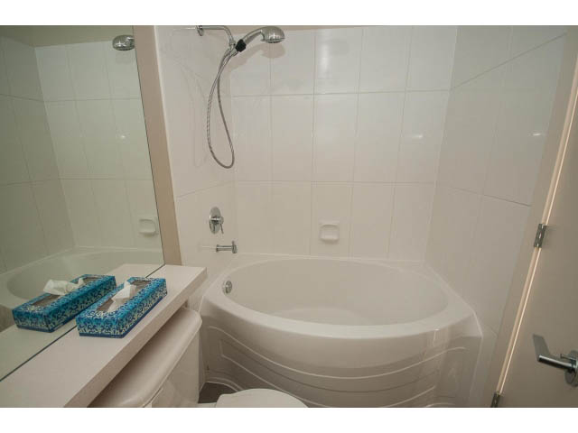 Furnished bathroom with white tiles and a curved bathtub. - 701 - 151 West 2nd Street, North Vancouver