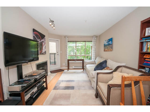 Furnished living room with a large TV, cozy sectional, and city view through the windows. - 201 - 150 West 22nd Street, North Vancouver