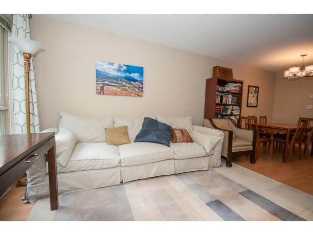 Furnished living room with white couches, wooden floor, and cityscape painting. - 201 - 150 West 22nd Street, North Vancouver