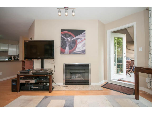 Living room with hardwood floors, a large TV, and a sliding glass door leading to a patio. - 201 - 150 West 22nd Street, North Vancouver