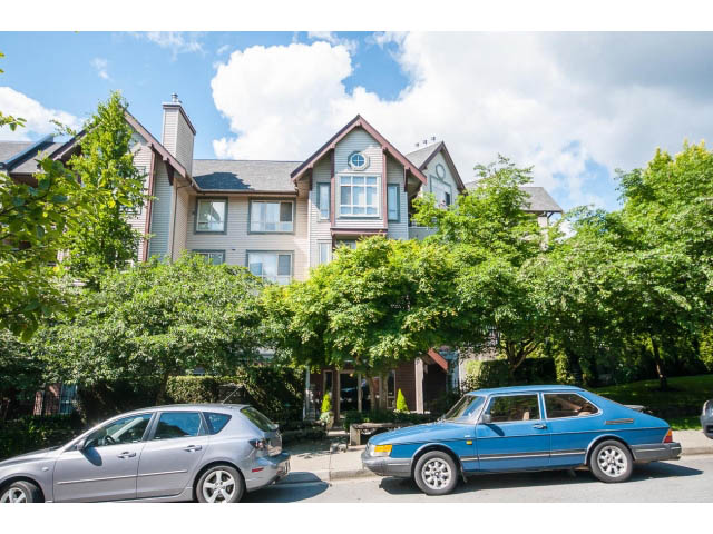 Bright living room with large windows, surrounded by lush greenery. - 201 - 150 West 22nd Street, North Vancouver
