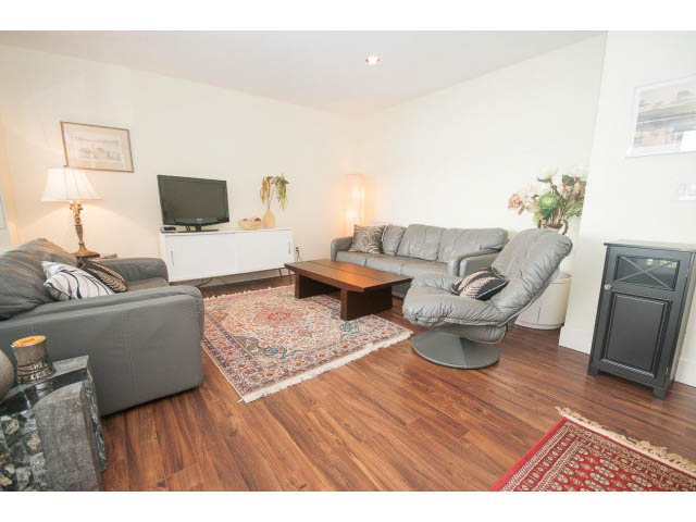 Furnished living room with hardwood floors, gray couch, and TV on white stand. - Suite - 2985 Dollarton Hwy, North Vancouver