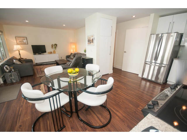 Bright dining area with modern chairs and glass table, hardwood floors, and a kitchen in the background. - Suite - 2985 Dollarton Hwy, North Vancouver