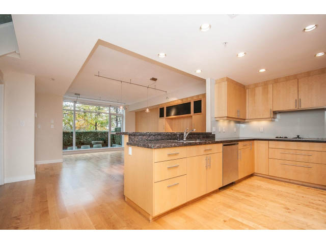 Bright kitchen with light wood cabinets, granite countertops, and hardwood floors, showcasing a modern city view.