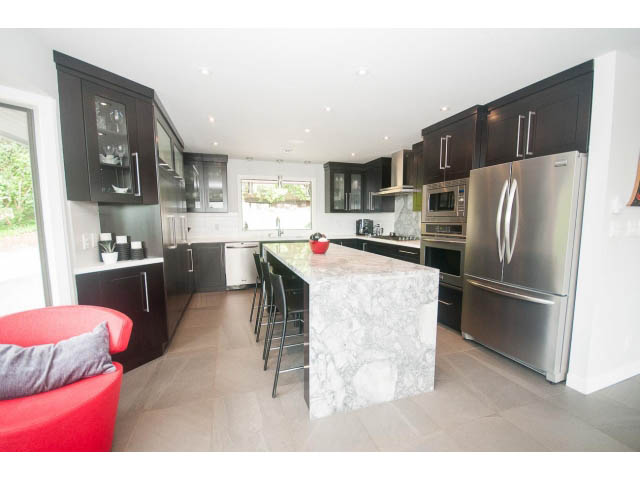 Bright kitchen with modern stainless steel appliances, granite countertops, and red accent furniture. - 2948 Marykirk Place, North Vancouver