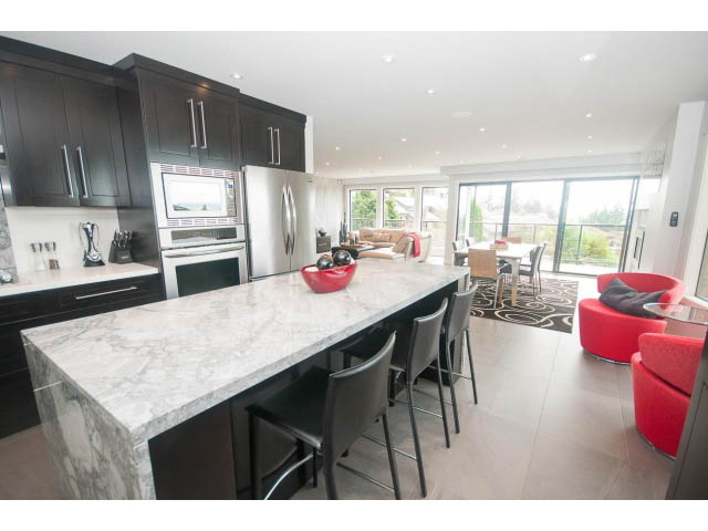 Bright kitchen with marble countertops and black cabinetry, leading to a spacious dining area with red chairs and a city...