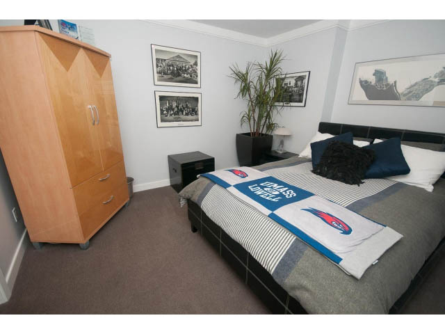 Furnished bedroom with striped bedding, wooden wardrobe, and framed artwork. - 2948 Marykirk Place, North Vancouver