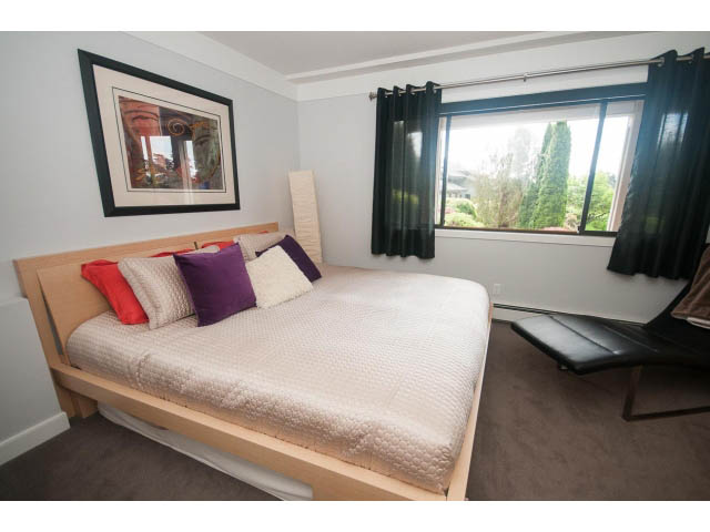 Bright bedroom with wooden bed, colorful pillows, and large window view. - 2948 Marykirk Place, North Vancouver
