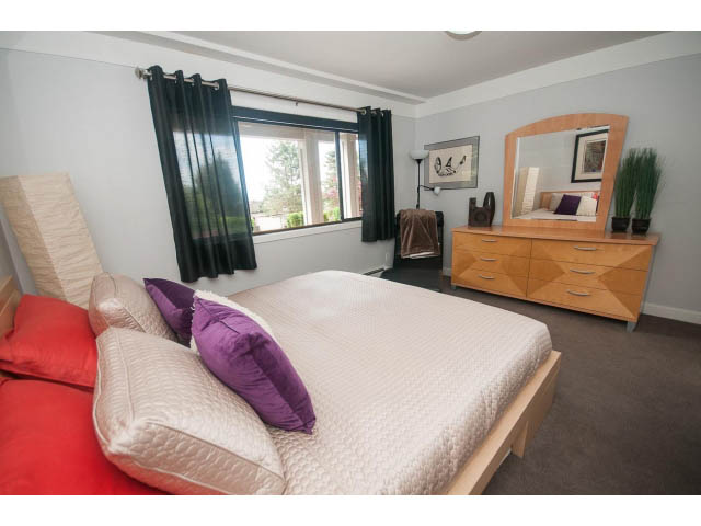 Bright bedroom with wooden furniture, purple and red bedding, and a city view. - 2948 Marykirk Place, North Vancouver