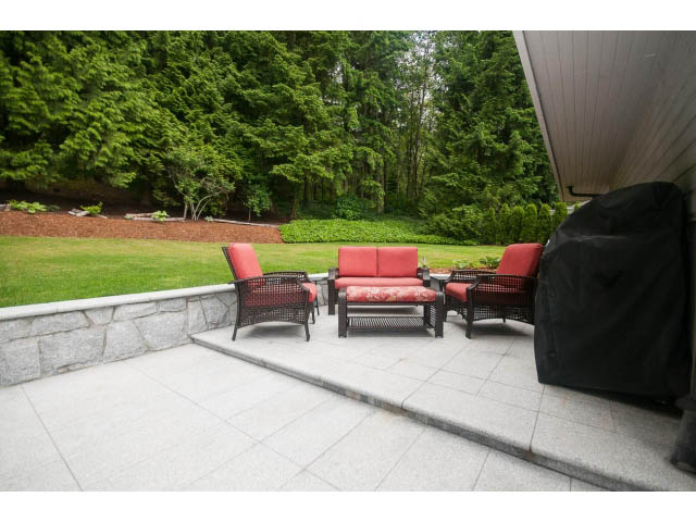 Furnished patio with red cushions, stone flooring, and lush greenery in the background. - 2948 Marykirk Place, North Vancouver